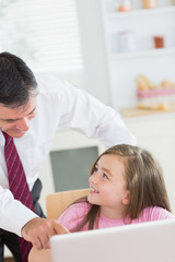 Father pointing at laptop with daughter smiling up at him