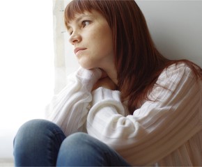 The sad young woman sits at a window