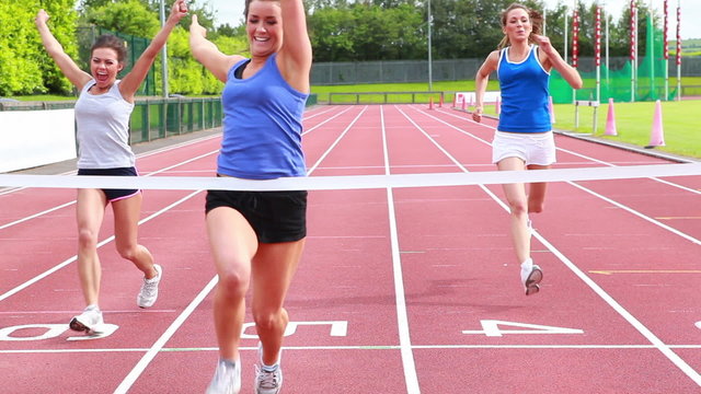 Three woman running on a track and crossing finish line