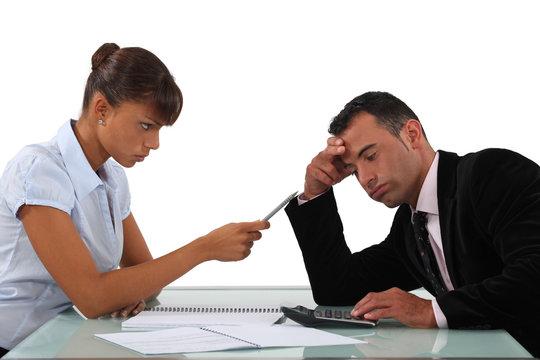 Stern woman with a man using a calculator