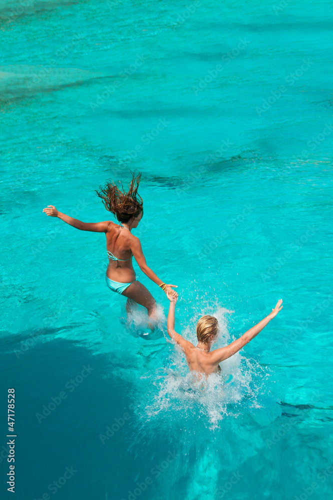 Wall mural Two girls jumping in the sea