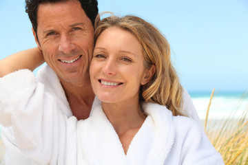 Obraz premium Happy couple wearing dressing gowns at the beach