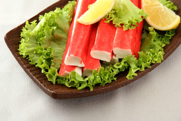 Crab sticks with lettuce leaves and lemon on plate, close up