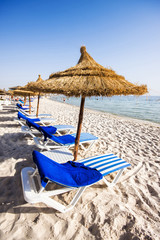 Belle plage avec chaises longues et parasols en chaume à Port El K