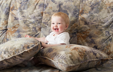 Fototapeta premium Happy baby girl sitting on a sofa