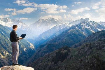 Naklejka premium Young businessman using his laptop on the mountain top