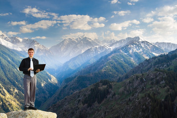 Young businessman using his laptop on the mountain top