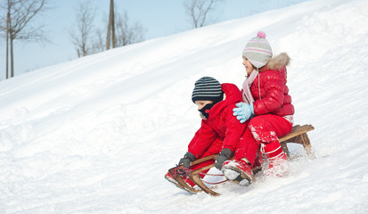 Two little kids - boy and girl - sliding with sledge in the snow