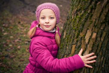 Little girl near tree in autumn or winter park.