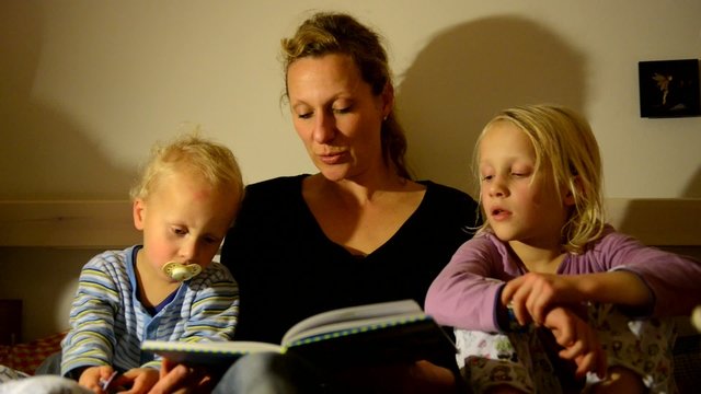 Mutter ließt Kindern im Bett eine Geschichte vor