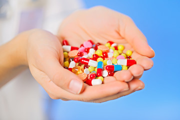 Pills, tablets and drugs heap in doctor's hand on blue backgroun