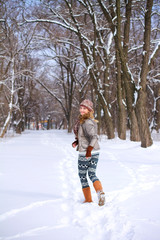 Fototapeta na wymiar Smiling girl running through the snow in a winter park outdoors
