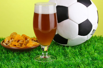 Glass of beer with soccer ball on grass on green background