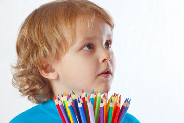 Young blond boy with color pencils on a white background