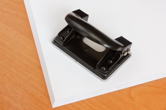 Black steel office hole punch and paper stack on desk
