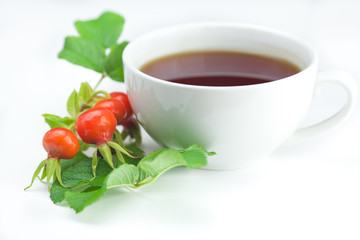 cup of tea and rosehip berries with leaves on white background