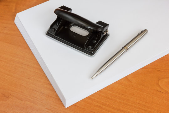 Black office hole punch and a pen on a paper stack
