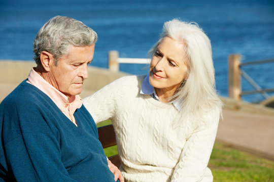 Senior Woman Comforting Depressed Husband Sitting On Bench