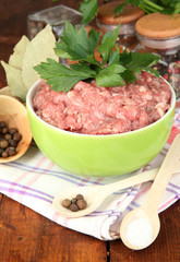 Bowl of raw ground meat with spices on wooden table