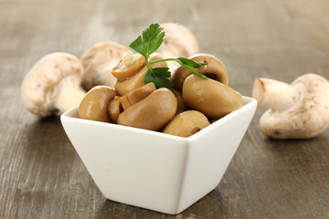 Delicious marinated mushrooms in bowl on wooden table close-up
