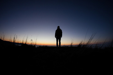 silhouette of man standing in field after sunset