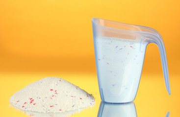 washing powder in a measuring cup, on yellow background