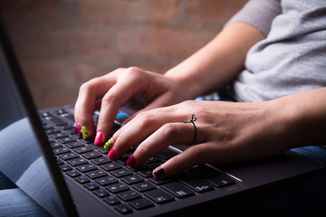 young woman with colorful nails typing on laptop keyboard