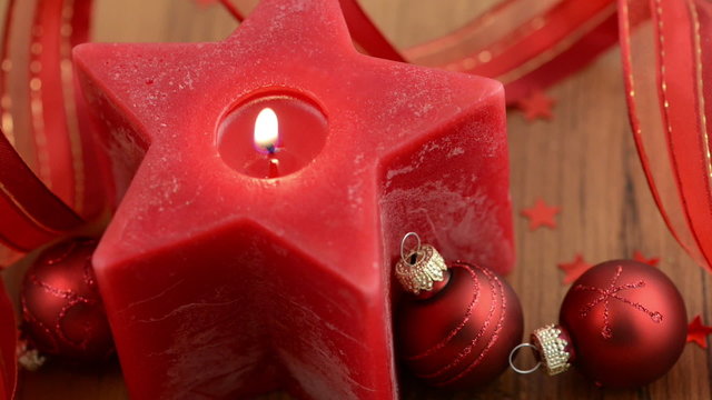 Sternf&ouml;rmige Kerze wird angez&uuml;ndet. Weihnachtsbaumkugeln.