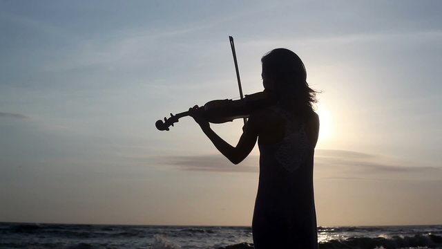 Silhouette of violinist playing on violin at ocean beach