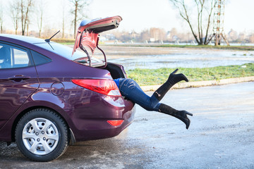 Woman swinging her legs into car luggage trunk