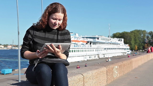Female student looking to laptop screen on city embankment