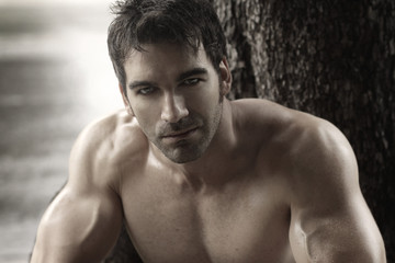 Sexy masculine man shirtless outdoors against tree