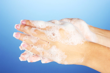 Woman's hands in soapsuds, on blue background close-up