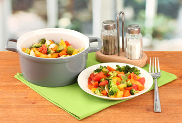 Vegetable stew in gray pot on wooden table on bright background