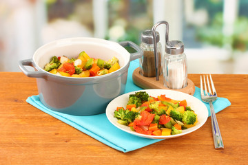 Vegetable stew in gray pot on wooden table on bright background