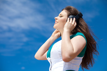 woman with headphones against the blue sky on beach
