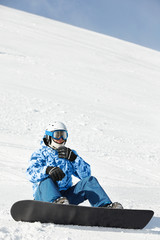 Fototapeta na wymiar Snowboarder w narciarskim kombinezonie i kasku siedzi na śnieżnym stoku