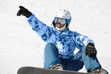 Fototapeta na wymiar Snowboarder w narciarskim kombinezonie i kasku siedzi na śnieżnym stoku