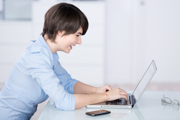 lächelnde frau im büro schaut auf ihren laptop
