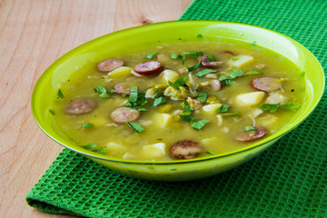 Pea soup with smoked sausages in a green plate