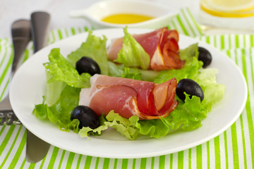 salad with prosciutto and olives on the plate and glass of water