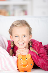 kind liegt mit sparschwein auf dem sofa