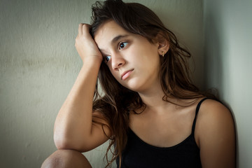 Sad hispanic girl sitting in a dark corner