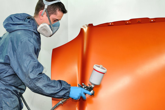 Worker painting orange car bonnet.