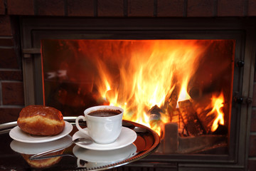 Kawa i pączek przed płonącym kominkiem.