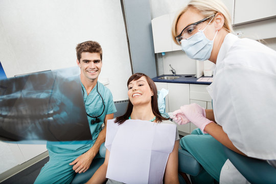Dentist With Female Assistant Showing X-Ray Image To Patient