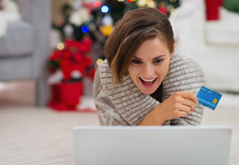 Surprised woman with laptop and credit card near Christmas tree