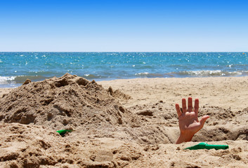 Man's hand out of the hole on the sandy beach
