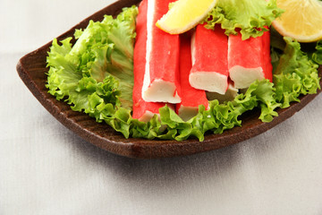 Crab sticks with lettuce leaves and lemon on plate, close up
