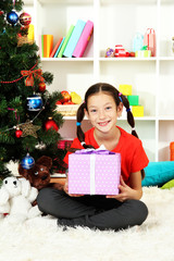 Obraz na płótnie Canvas Little girl holding gift box near christmas tree